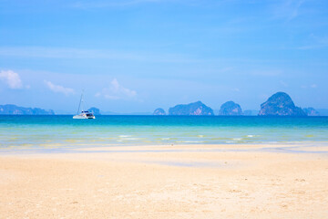 Seascape. Sandy beach with boat in azure sea water and islands in the sea on the horizon in Krabi...