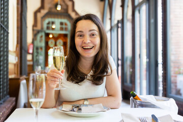 Young positive woman holding glass of white wine in restaurant