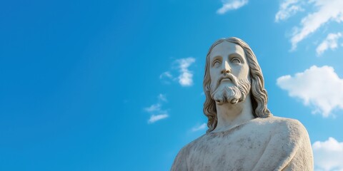Fototapeta premium A statue of Jesus is standing in front of a blue sky. The statue is made of stone and is very detailed. The sky is clear and bright, creating a peaceful and serene atmosphere
