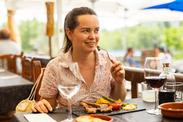 Woman seating at table in restaurant and eating lamb dish. Portrait of woman enjoying her meal. © JackF