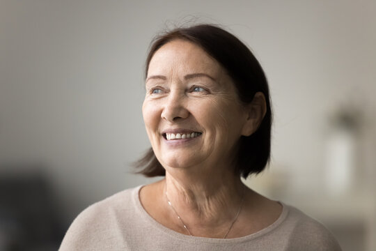 Smiling pretty mature female looks into distance with gentle smile, close up head shot portrait of optimistic older woman casually dressed stare aside with dreamy expression. Future, nostalgia, recall