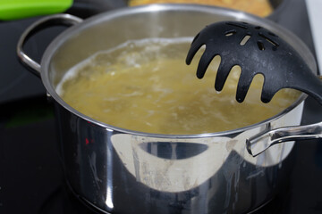 Cooking Pasta in a Stainless Steel Pot on Stove. Close-up of pasta boiling in a stainless steel pot with a pasta spoon, perfect for cooking and food concepts.