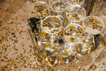 Champagne glasses elegantly arranged on a mirrored table, filled with sparkling wine and decorated with gold confetti, creating a luxurious and celebratory ambiance.