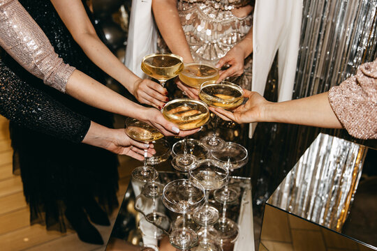 A toast among elegantly dressed women holding coupe glasses filled with champagne
