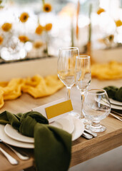 Elegant table setting with glassware, white plates, green knotted napkins, and a yellow name card, surrounded by warm-toned floral decor in a bright and stylish event space.