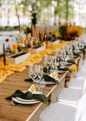 A beautifully decorated wedding reception table with elegant place settings, white plates, green...