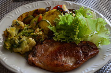 Healthy and nutritious food, various vegetables, many nutrients, zucchini, eggplant, tomatoes, carrots, cauliflower, broccoli, colorful peppers, lettuce and steak, well-cooked and juicy pork protein.