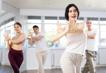 Fototapeta premium Happy emotional sporty young female dancer rehearsing popping techniques during group workout in modern street dance studio