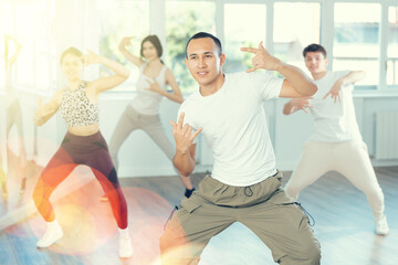 Positive smiling young man dancing hip hop with group of guys and girls in modern dance class