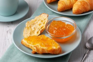Freshly baked croissants served with jam and coffee on a light wooden table