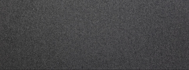A close-up of dark gray paper, focusing on its smooth surface with subtle graininess. The plain background enhances the details and texture in the foreground, highlighting the paper’s quality