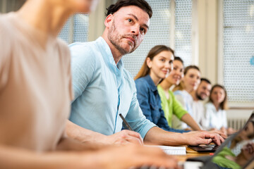 Fototapeta premium Portrait of a student guy with fellow students, studying on a laptop and writing a synopsis lecture in copybook during class ..in a university auditorium