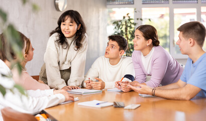 Friendly interested young Asian female student taking part in group discussion of study topics with coursemates