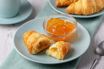 Freshly baked croissants served with jam and coffee on a light wooden table
