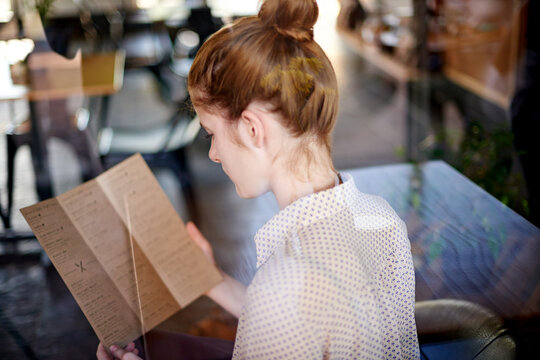 Cafe, woman and reading with menu, food decision or beverage choice. Girl, back and lunch with options of restaurant for hunger, snack or meal at coffee shop or bistro for hungry customer order