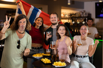 Group of friends fans watching match cheering with Norwegian flag in bar