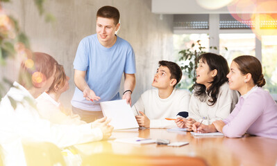 Young male tutor teaching group of students in college