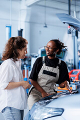 Trained mechanic helping client with car maintenance in auto repair shop. Employee in garage...