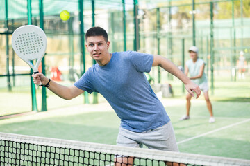Caucasian teenage boy in sportswear playing padel tennis match during training on court.