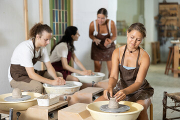 In workshop, girl sits near potter wheel and makes pottery. Handmade products, creativity and variety of activities, ancient craft as modern hobby, craze for pottering, devotion to pottering
