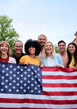 Vertical. Multiracial group of friends holding the American flag with pride, celebrating Independence Day outdoors. Joyful atmosphere with a sense of unity and patriotism in a vibrant summer setting