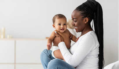 African Mother And Baby Portrait. Profile Side View Of Happy Black Mommy Holding And Playing With Her Adorable Little Infant In Diaper, Free Copy Space, Banner, Selective Focus, Blurred Background
