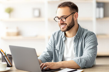 Happy young guy with flag of the US working at desk with laptop in home office. Millennial male student learning English online for foreign job, education or emigration to America