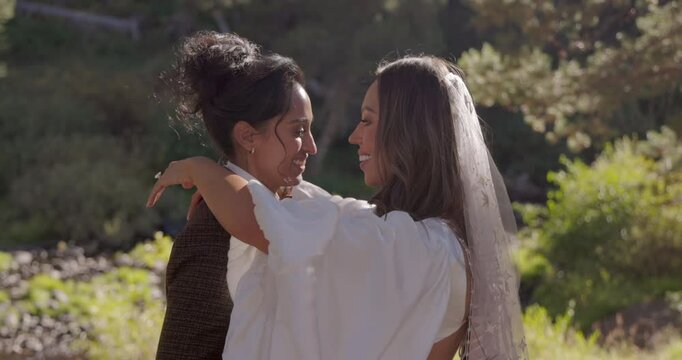 Beautiful multiethnic lesbian couple joyfully celebrates their wedding day in a picturesque outdoor setting, two brides kissing each other, they express their love and happiness on special occasion