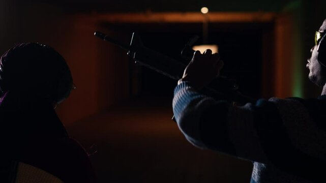 Man holds rifle, enjoying recreational shooting experience in firing range next to group of friends. People practicing with weapons in safe environment at shooting range company, camera B