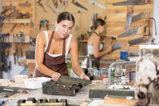 Interested young woman in pinafore examining metal template in carpentry workroom