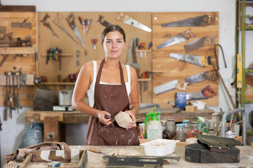Positive young girl in apron posing cheerfully in carpentry workshop