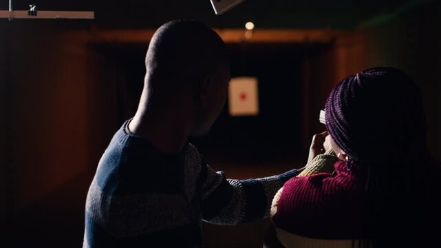 Shooting gallery staff member teaching student how to hold and handle handgun. Firing range expert providing guide to african american woman learning how to achieve proficiency with guns, camera B