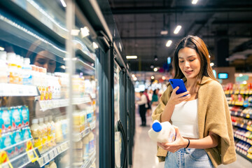 Happy Asian woman using mobile phone, shopping buying food and grocery at supermarket. Customer...
