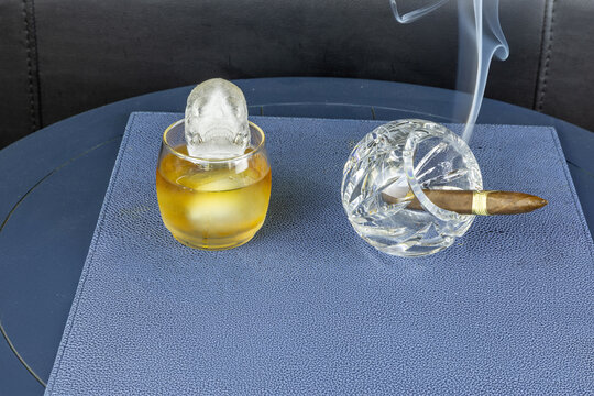 Smoking cigar in a crystal ash tray next to a glass of whisky