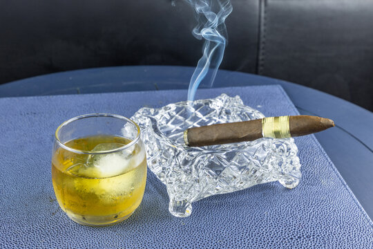 Smoking cigar in a crystal ash tray next to a glass of whisky
