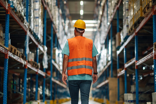 Warehouse worker walking through large distribution warehouse with shelves full of goods