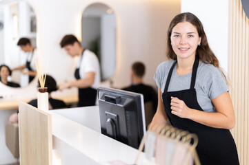 Young female hairdresser stylist stands at cash register in beauty salon