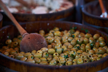 Close-up of olives in a wooden container at a bustling market stall in early morning light