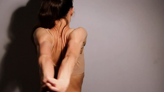 Sport woman doing stratching exercises for shoulders, scapula and healthy upper back, holds hands in a lock and moves hands from side to side. Female model in bra on studio low key shadow. Back view