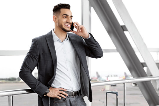 Mobile Communication. Handsome Middle Eastern Man Talking On Cellphone In Airport, Cheerful Young Arab Man Enjoying Pleasant Phone Conversation While Waiting For Departure In Terminal, Free Space