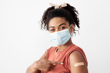 African american young woman with face mask posing after immunization, showing her shoulder with band on, black lady got vaccinated, immunization during coronavirus pandemic, closeup, isolated