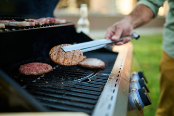 Man grilling hamburgers and sausages on backyard barbecue