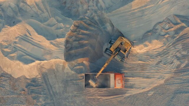 Aerial Top Down View of Excavator Loading Dump Truck with Gravel in Quarry During Golden Sunset Hour