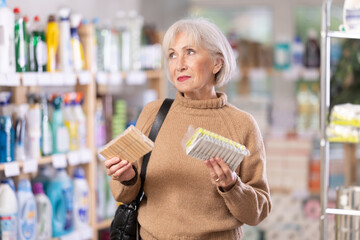 Elderly woman chooses clothespins - wooden or plastic, in a hardware store