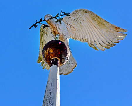 Weathered and worn, with chipped white paint wooden peace dove topping a church steeple lightning rod