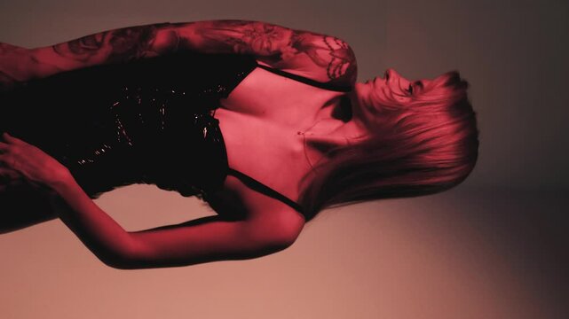 Blonde with a beautiful figure in a black patent leather bodysuit poses in a studio. Studio lighting, low exposure, monochrome red light