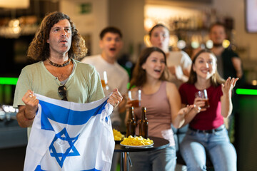 Group of friends fans watching match cheering with Israeli flag in bar