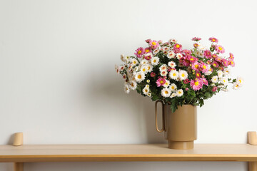 Vase with beautiful flowers on wooden shelf near white wall, space for text