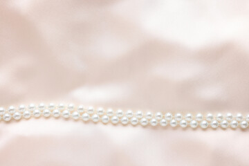 Beautiful pearl necklace on beige cloth, top view. Space for text