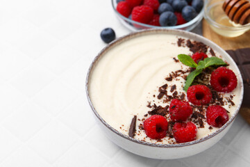 Tasty cooked semolina porridge with berries served on white tiled table, closeup. Space for text